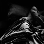 A man lying in bed in tumbled sheets.