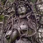 An angel statue tangled in vines.