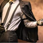 A man wearing leather gloves and suspenders, with his suit jacket draped across his shoulders. He's striking a cocky pose.