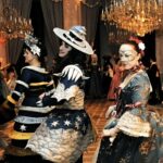 Costumed attendees at a masquerade ball look back at the camera.