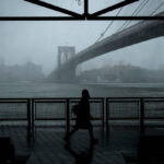 A photo of the Brooklyn Bridge from the East River Greenway, in fog at twilight.